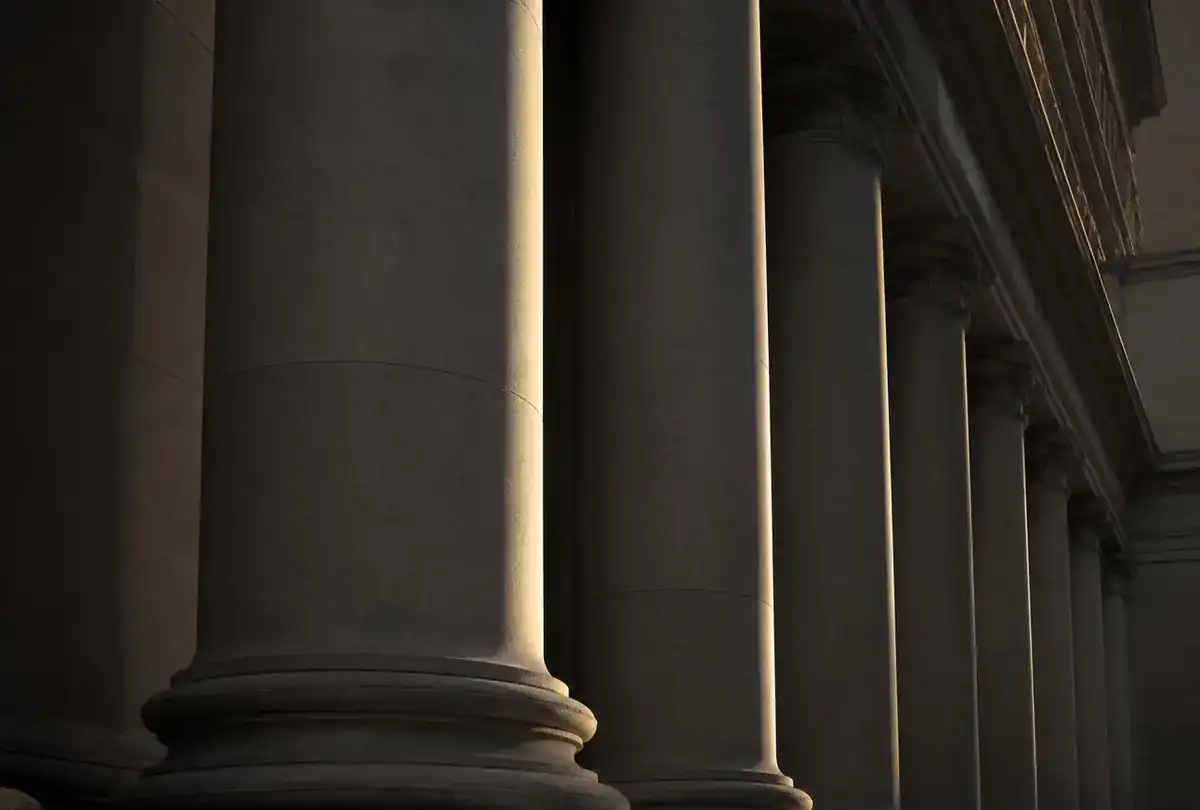 Colunata de fórum em pedra com luz rasante, representando o contexto judicial
